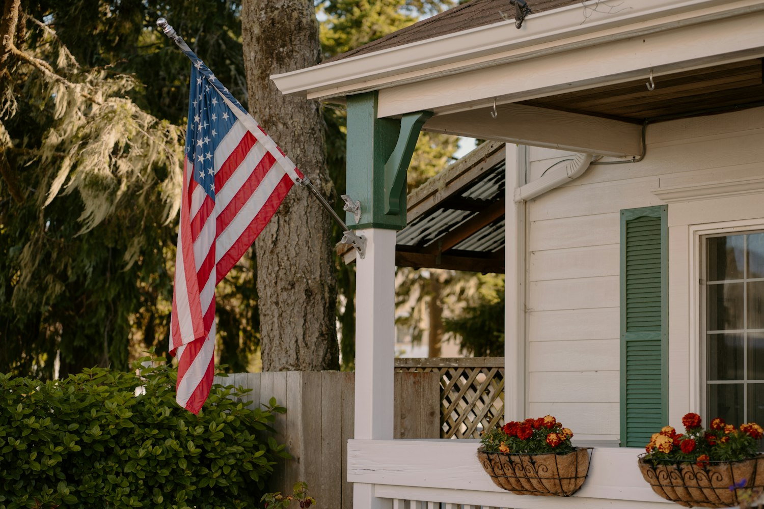 An American flag on the porch of a white farmhouse in golden light