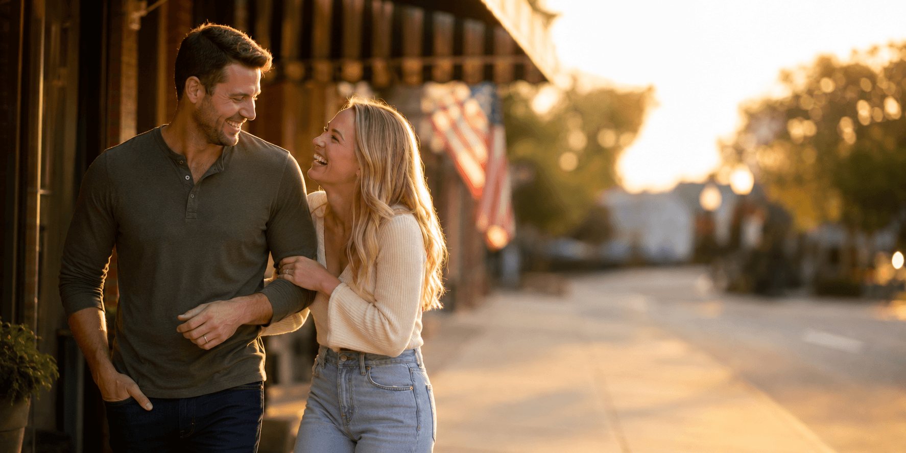 A man and woman laughing together on a small-town street at golden hour